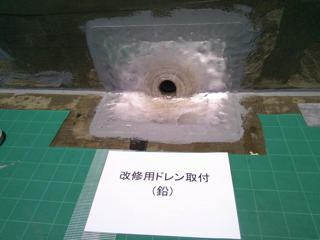 改修用ドレン(鉛)取付の様子。<br />
既存のドレン穴が少し高い位置にあったのと、既存より口径が小さくなるので、排水能力は低下しますがドレン排水口も2箇所あり、全体的に勾配もしっかりついているため、特に問題ないかと思います。